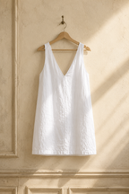 White linen shift mini dress, hanging on wooden hanger against plaster wall