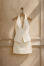 Cream cotton mini mini dress, hanging on wooden hanger against plaster wall