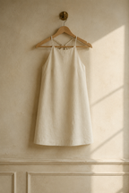 Ivory linen shift mini dress, hanging on wooden hanger against plaster wall