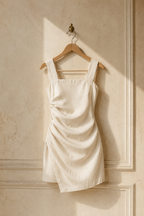 Ivory linen draped mini dress, hanging on wooden hanger against plaster wall
