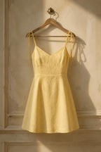 Butter yellow linen a-line mini dress, hanging on wooden hanger against plaster wall