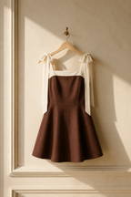 Brown linen a-line mini dress, hanging on wooden hanger against plaster wall