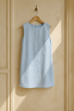 Light blue linen shift mini dress, hanging on wooden hanger against plaster wall