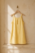 Butter yellow linen shift mini dress, hanging on wooden hanger against plaster wall