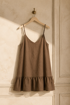 Brown linen slip mini dress, hanging on wooden hanger against plaster wall