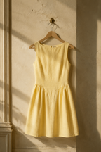 Butter yellow linen a-line mini dress, hanging on wooden hanger against plaster wall