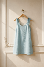 Light blue linen shift mini dress, hanging on wooden hanger against plaster wall