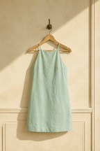 Mint green linen shift mini dress, hanging on wooden hanger against plaster wall