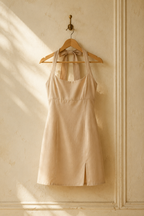 Beige cotton a-line mini dress, hanging on wooden hanger against plaster wall