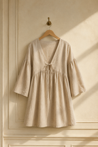 Beige linen a-line mini dress, hanging on wooden hanger against plaster wall