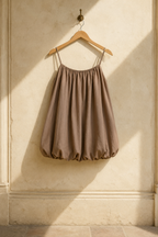 Taupe cotton bubble mini dress, hanging on wooden hanger against plaster wall