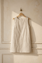 Light beige linen shift mini dress, hanging on wooden hanger against plaster wall