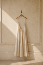 Cream linen slip maxi dress, hanging on wooden hanger against plaster wall