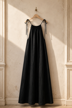 Black linen slip maxi dress, hanging on wooden hanger against plaster wall