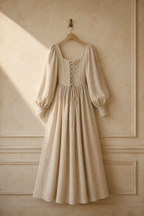 Beige linen a-line maxi dress, hanging on wooden hanger against plaster wall