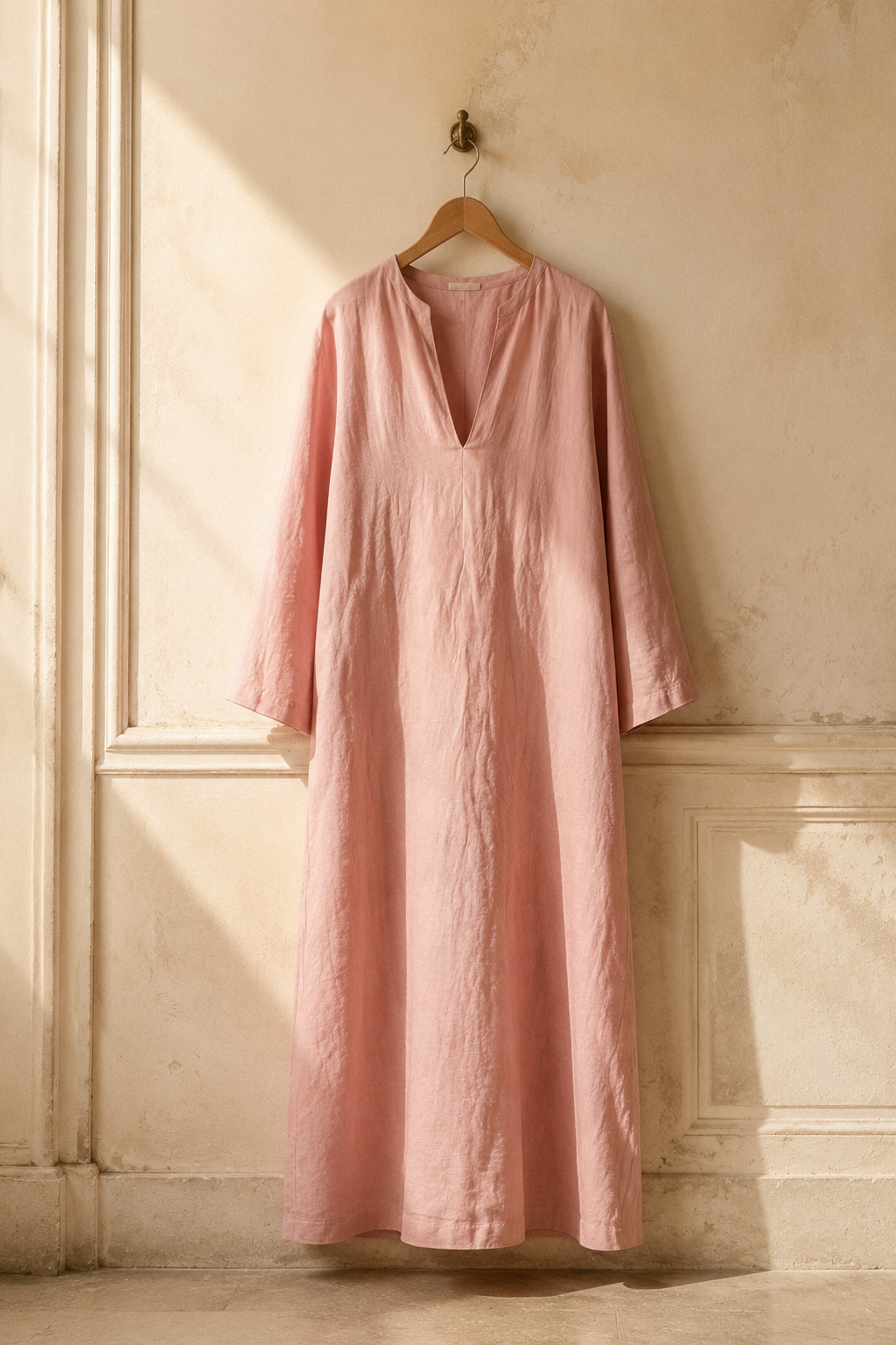 Dusty pink linen shift maxi dress, hanging on wooden hanger against plaster wall