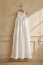 White linen shift maxi dress, hanging on wooden hanger against plaster wall