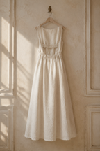 Ivory linen a-line maxi dress, hanging on wooden hanger against plaster wall