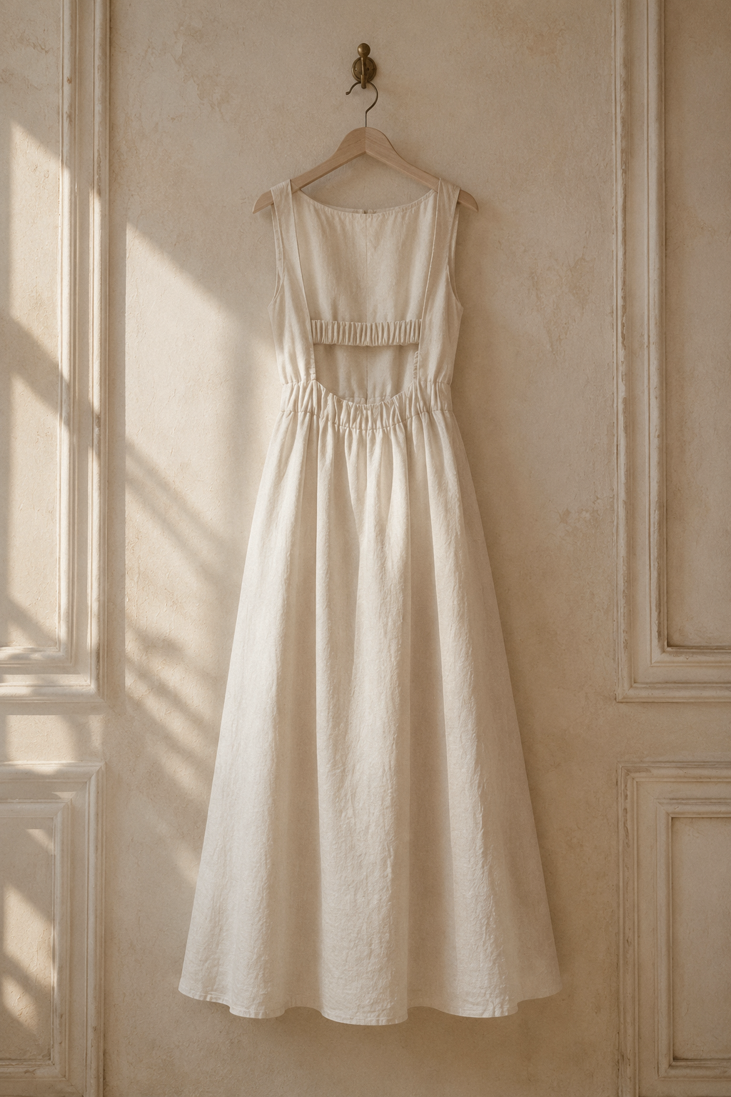 Ivory linen a-line maxi dress, hanging on wooden hanger against plaster wall