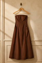 Brown cotton a-line maxi dress, hanging on wooden hanger against plaster wall