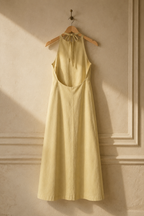 Pale yellow linen shift maxi dress, hanging on wooden hanger against plaster wall