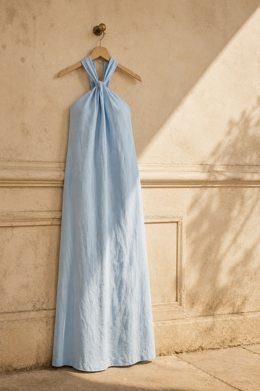 Light blue linen shift maxi dress, hanging on wooden hanger against plaster wall