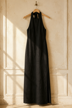 Black linen column maxi dress, hanging on wooden hanger against plaster wall