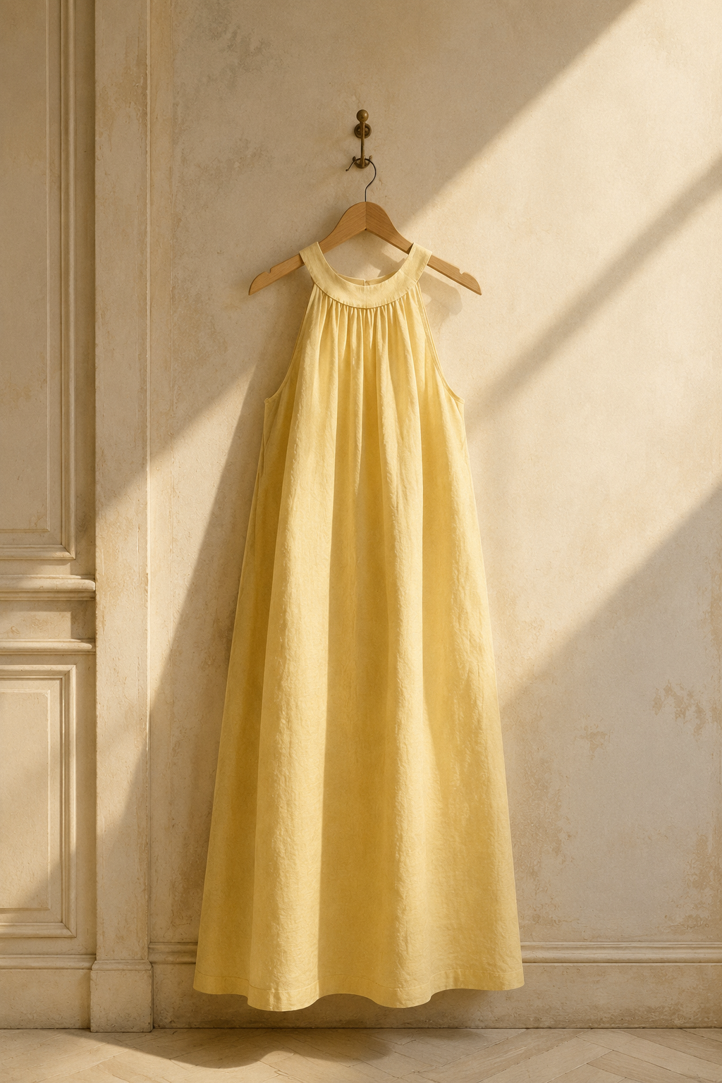 Butter yellow linen shift maxi dress, hanging on wooden hanger against plaster wall
