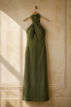 Olive green linen column maxi dress, hanging on wooden hanger against plaster wall