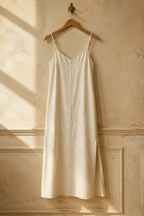 Ivory linen slip maxi dress, hanging on wooden hanger against plaster wall