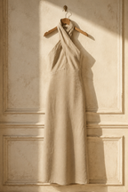 Beige linen column maxi dress, hanging on wooden hanger against plaster wall