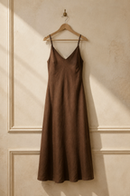 Brown linen slip maxi dress, hanging on wooden hanger against plaster wall