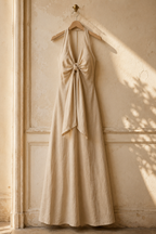 Beige linen a-line maxi dress, hanging on wooden hanger against plaster wall