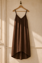 Brown linen slip maxi dress, hanging on wooden hanger against plaster wall