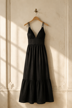 Black linen tiered maxi dress, hanging on wooden hanger against plaster wall