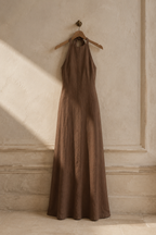 Brown linen column maxi dress, hanging on wooden hanger against plaster wall
