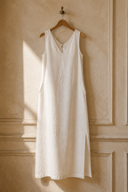 Ivory linen shift maxi dress, hanging on wooden hanger against plaster wall
