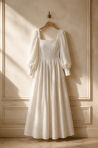 Ivory linen a-line maxi dress, hanging on wooden hanger against plaster wall