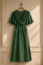 Green linen wrap maxi dress, hanging on wooden hanger against plaster wall