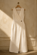 Ivory linen wrap maxi dress, hanging on wooden hanger against plaster wall