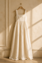 Ivory linen a-line maxi dress, hanging on wooden hanger against plaster wall