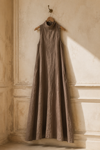 Taupe linen a-line maxi dress, hanging on wooden hanger against plaster wall