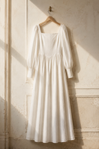 Ivory linen a-line maxi dress, hanging on wooden hanger against plaster wall