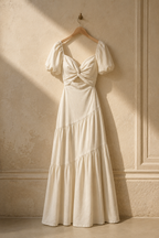 Ivory linen tiered maxi dress, hanging on wooden hanger against plaster wall