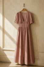 Dusty rose linen a-line maxi dress, hanging on wooden hanger against plaster wall