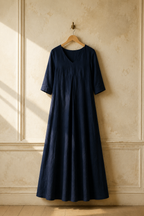 Navy blue linen a-line maxi dress, hanging on wooden hanger against plaster wall