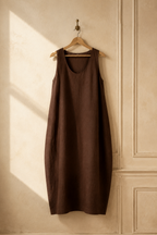 Dark brown linen shift maxi dress, hanging on wooden hanger against plaster wall