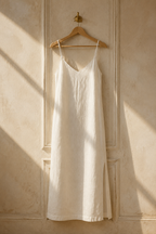 Ivory linen slip maxi dress, hanging on wooden hanger against plaster wall