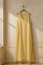 Butter yellow linen shift maxi dress, hanging on wooden hanger against plaster wall