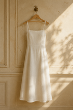 Ivory linen a-line maxi dress, hanging on wooden hanger against plaster wall